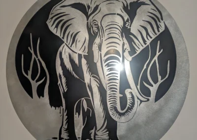 Circular metal art piece depicting an elephant with foliage, using negative space design