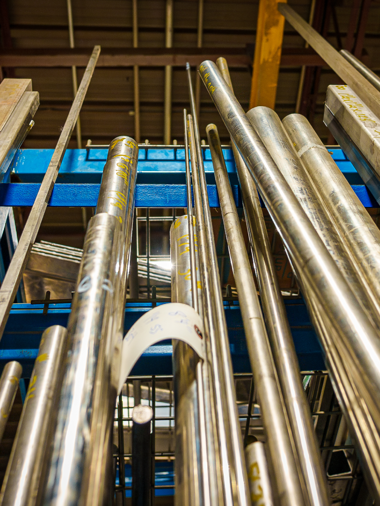 Metal pipes stored vertically in a rack, with industrial background